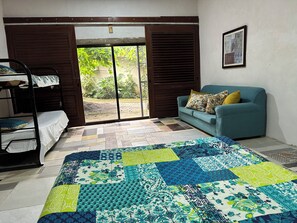 A room with a bunk bed, a sofa with floral cushions, a quilt with a patchwork design, and a door leading to an outdoor area. - Delightful 1-bedroom fully equipped cabin in Nuevo Colón welcomes your stay! (Nuevo Colón)