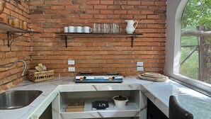 A kitchen with a brick wall, a gas stove, a sink, and a window with a view. - Delightful 1-bedroom fully equipped cabin in Nuevo Colón welcomes your stay! (Nuevo Colón)