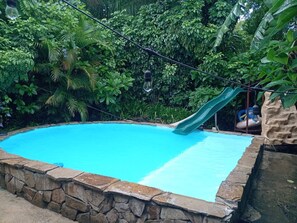 A swimming pool with a slide, surrounded by lush greenery. - Delightful 1-bedroom fully equipped cabin in Nuevo Colón welcomes your stay! (Nuevo Colón)