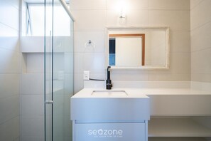 Ein modernes Badezimmer mit Duschkabine aus Glas, einem weißen Waschbecken und einem Spiegel mit Holzrahmen.