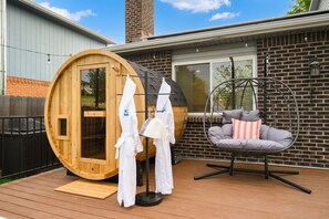 Una sauna a botte in legno, una sedia sospesa con cuscini e un pontile in legno.