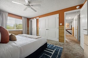 A bedroom with a bed, a ceiling fan, a window with curtains, and a hallway leading to another room. - Rangewell Retreat: Hot Tub, Sauna, Fire Pit, Games for Groups & Families (Arvada)