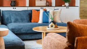 Ein Wohnzimmer mit einem blauen Sofa, einem runden Holztisch und einem rosa Sessel.