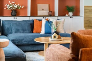 A living room with a blue sofa, a round wooden coffee table, and a pink armchair. - Rangewell Retreat Hot Tub, Sauna, Fire Pit, Games, Groups & Families (Arvada)