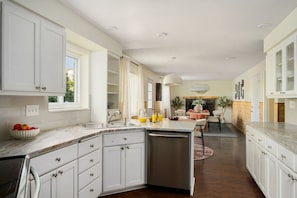 A kitchen with white cabinets, a built-in dishwasher, and a dining area with a table and chairs. - Rangewell Retreat Hot Tub, Sauna, Fire Pit, Games, Groups & Families (Arvada)