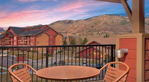 A balcony with wicker chairs, a view of a mountain range, and a red building in the background. - Relaxing 3 bedroom resort in amazing Steamboat Springs with amenities! (Steamboat Springs)