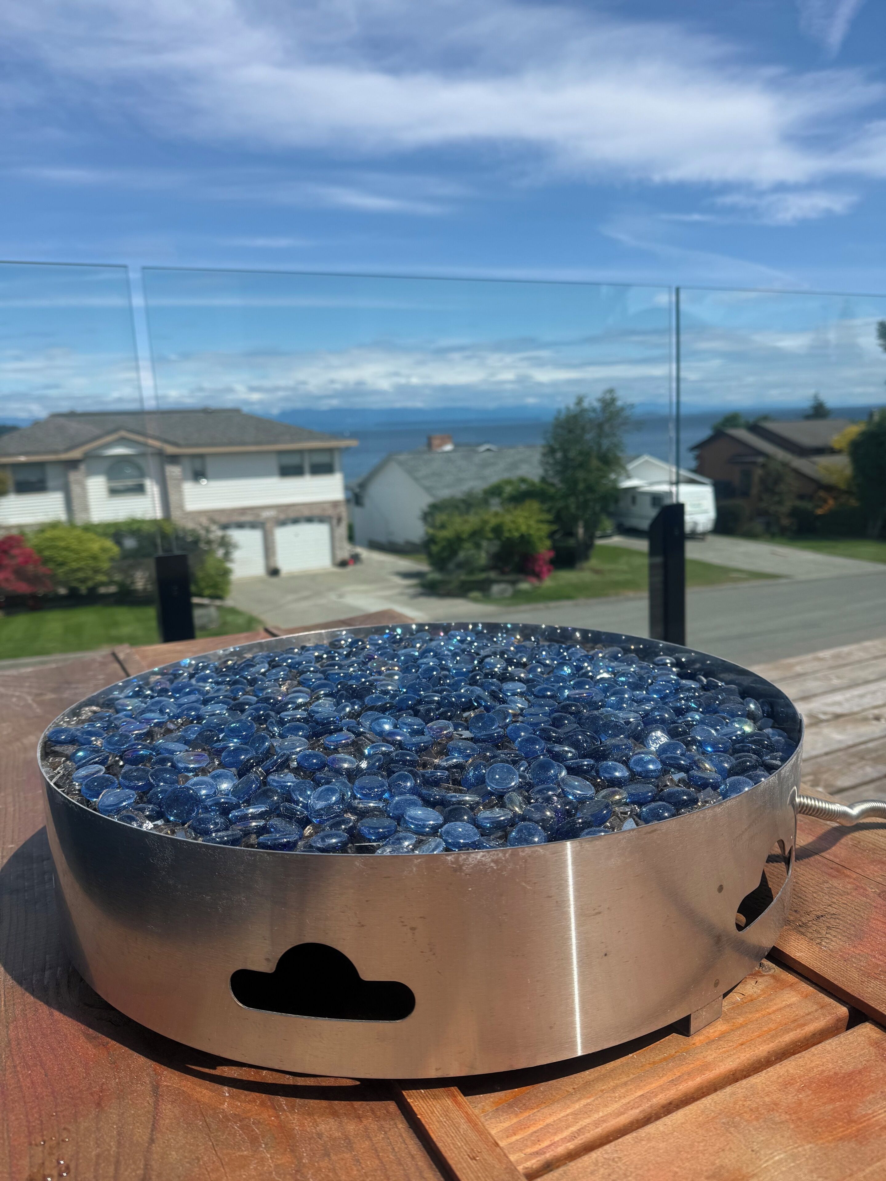 Un recipiente metálico redondo lleno de piedras de vidrio azules sobre una superficie de madera.