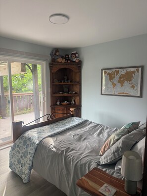 A bedroom with a bed, a wooden cabinet with decorative items, a world map on the wall, and a view of the outdoors through a glass door. - Passage view 2,0
Close to beaches and shopping, pet friendly and family friendly (Campbell River)