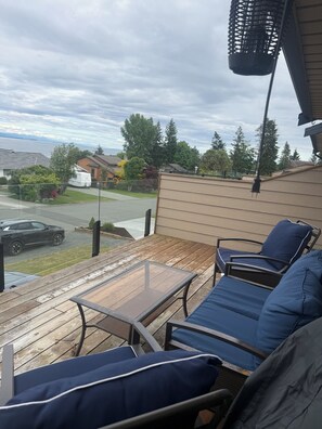 En uteplats med utemöbler, utsikt över en bostadsgata och en vattenyta i bakgrunden.