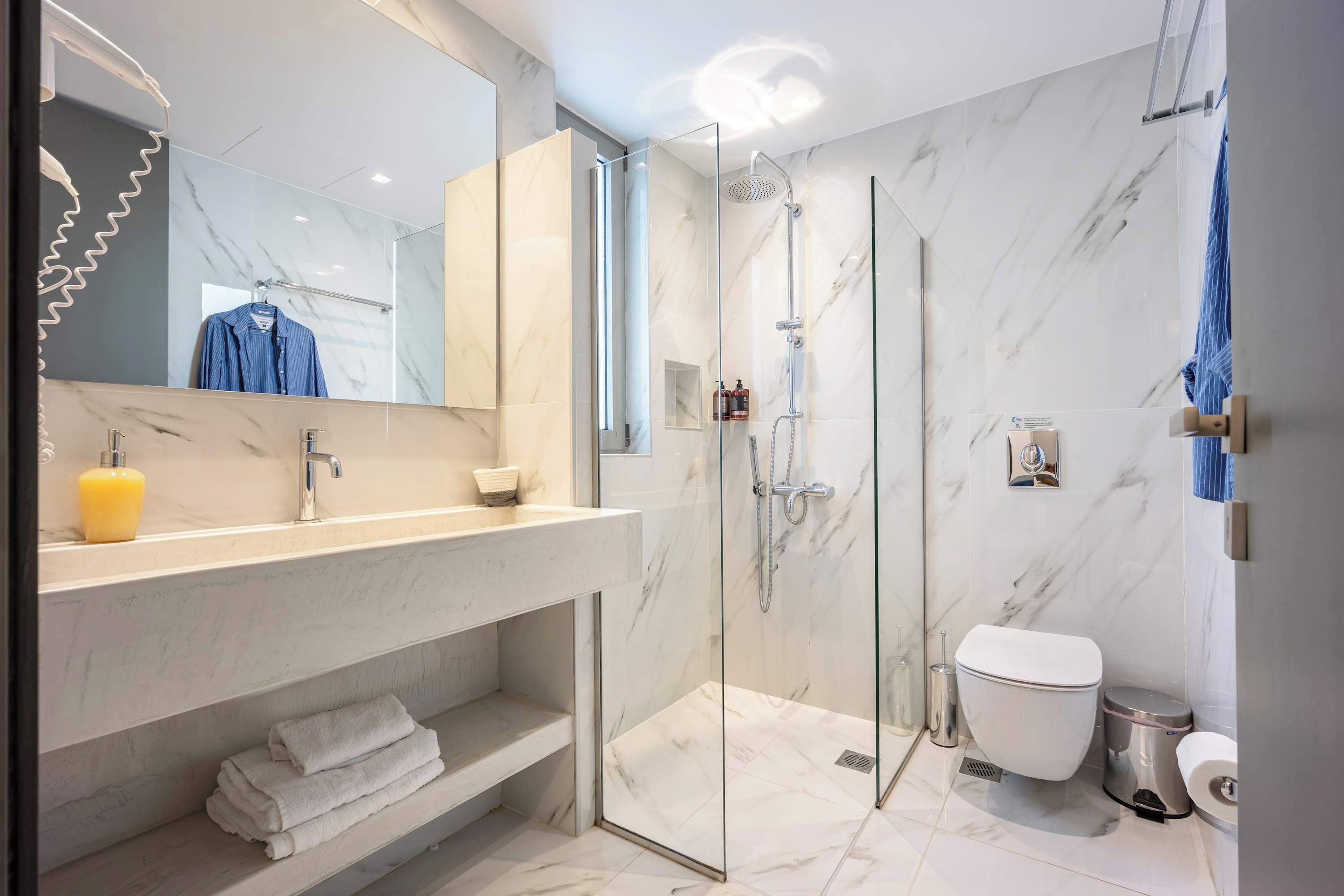 Un baño moderno con cabina de ducha de vidrio, suelo de baldosas de mármol, inodoro blanco y tocador con espejo y toallero.