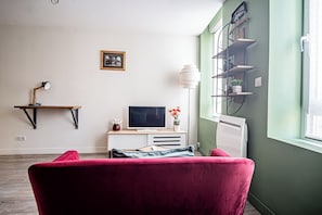 A room with a red chair, a TV, a white cabinet, a shelf with plants, and a picture on the wall. - Vrbo Property (Reims)