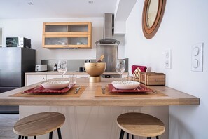 A modern kitchen with a central island, wooden cabinets, a stainless steel range hood, and a large mirror above the island. - Vrbo Property (Reims)