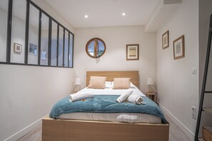 A bedroom with a bed, a round mirror, framed pictures, and a wooden headboard. - Vrbo Property (Reims)