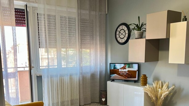 A living room with a sofa, a TV, a plant, and a wall clock. - A Due Passi Dalla Certosa via Guglielmo Marconi 12, Certosa di Pavi (Certosa di Pavia)
