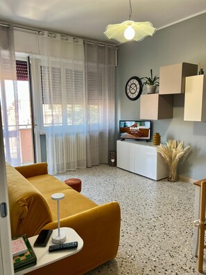 En stue med sofa, fjernsyn, en plante og et vægur.