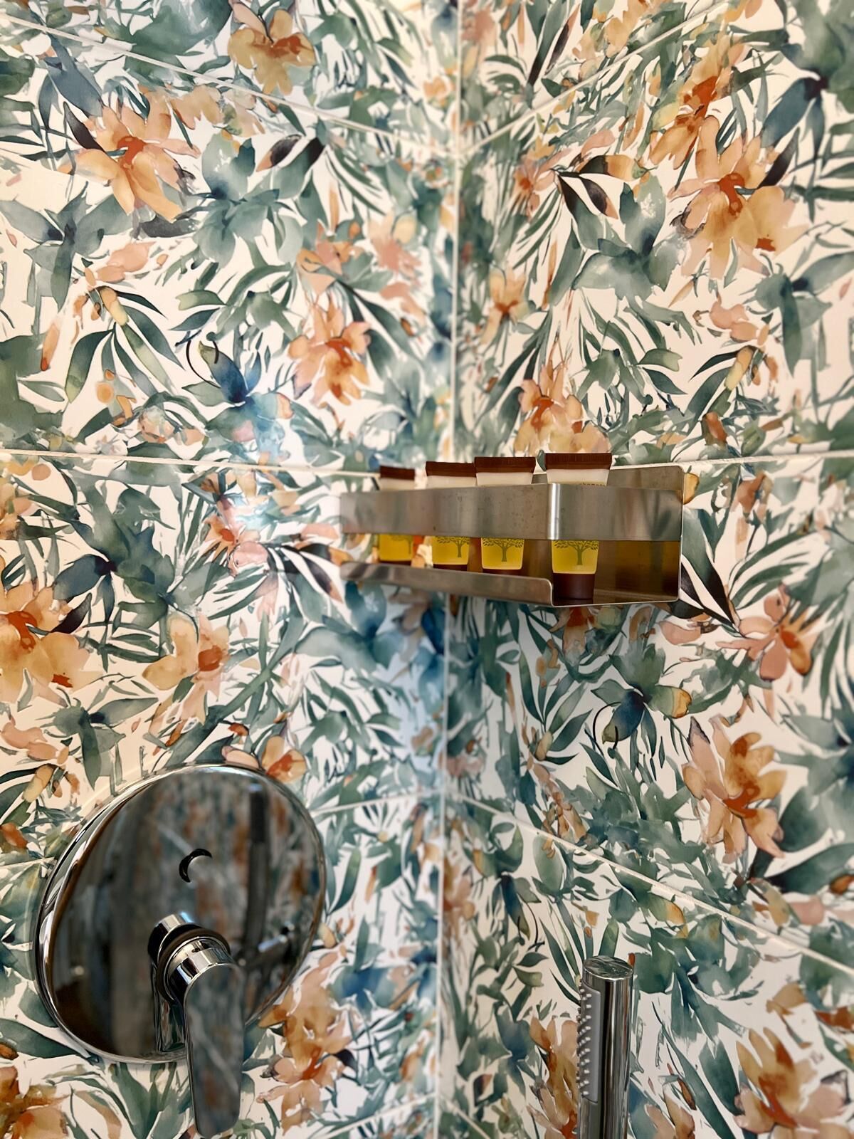 Een badkamer met bloemenbehang, een moderne kraan en een houten plank met decoratieve objecten.