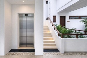 Ein modernes Interieur mit einem metallenen Aufzug, einer Treppe mit Holzhandläufen und einer sauberen, weißen Wand.