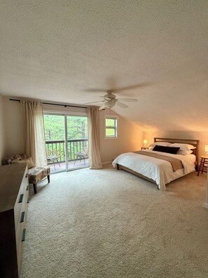 A bedroom with a bed, a ceiling fan, a window, and a view of greenery outside.