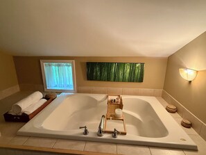 Eine große Badewanne mit einem hölzernen Tablett, einem Handtuch und einem Fenster mit Vorhängen.