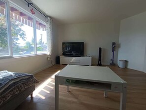 Una habitación con cama, televisor en un mueble, una mesa y una ventana con cortinas.