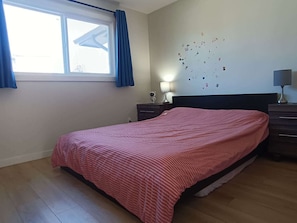 Une chambre à coucher comprenant un lit, une table de chevet, une lampe, une commode, une fenêtre avec des rideaux et des éléments décoratifs sur les murs.