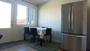 A compact kitchen with a dining table, chairs, a refrigerator, and a window.
