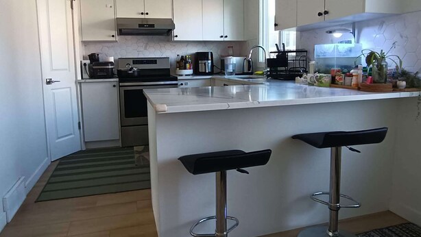 A modern kitchen with white cabinets, a stainless steel range, a built-in oven, a coffee maker, and a bar area with stools.