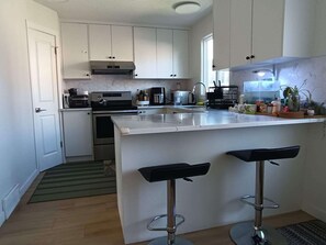 A modern kitchen with white cabinets, a stainless steel range, a built-in oven, a coffee maker, and a bar area with stools. - Full privacy whole Unit 4+ bedrooms next to downtown & airport (CALGARY)