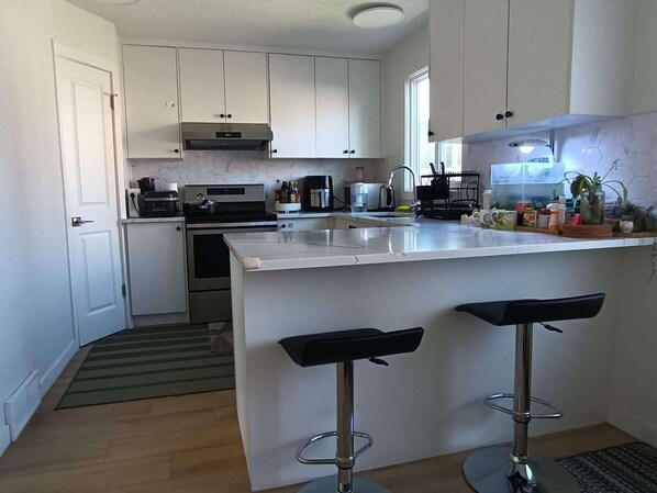 A modern kitchen with white cabinets, a stainless steel range, a built-in oven, a coffee maker, and a bar area with stools.