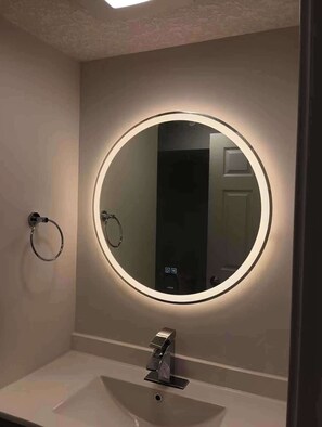 Un baño con un espejo redondo, un perchero para toallas y un lavabo.