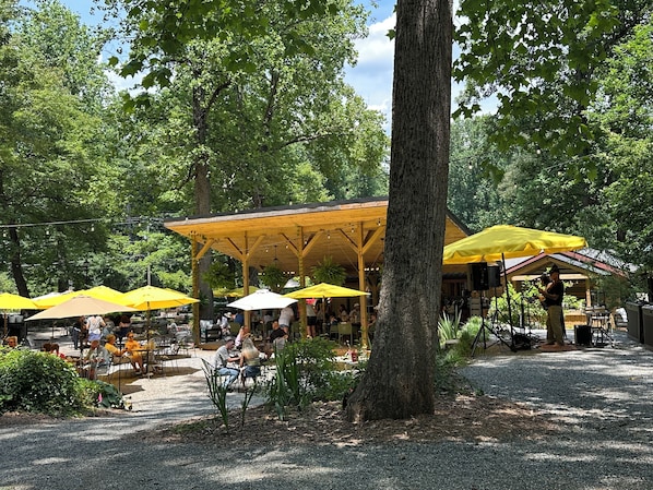 An outdoor seating area with tables and yellow umbrellas, surrounded by trees.