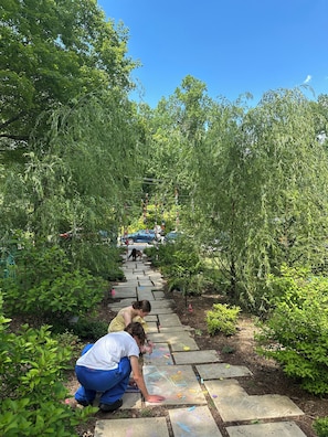 A pathway surrounded by greenery, leading to a parking area with cars.