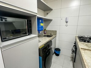 A compact kitchen with a microwave, water dispenser, sink, and a stove.
