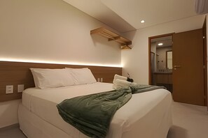 A hotel room with a bed, a wooden headboard, a nightstand, a mirror, and a door. - Cond em Resort Pe na Areia - By MME (Maceió)