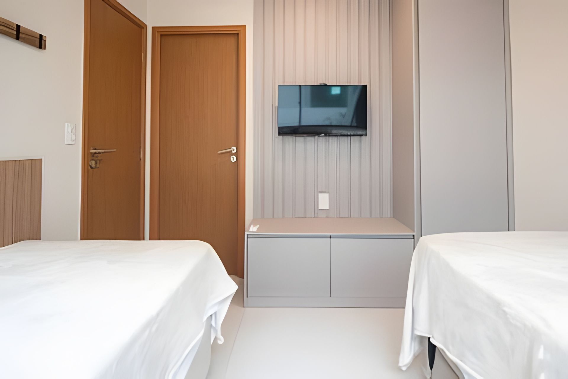 Et hotelværelse med to senge, et fjernsyn ophængt på væggen og en trædør.