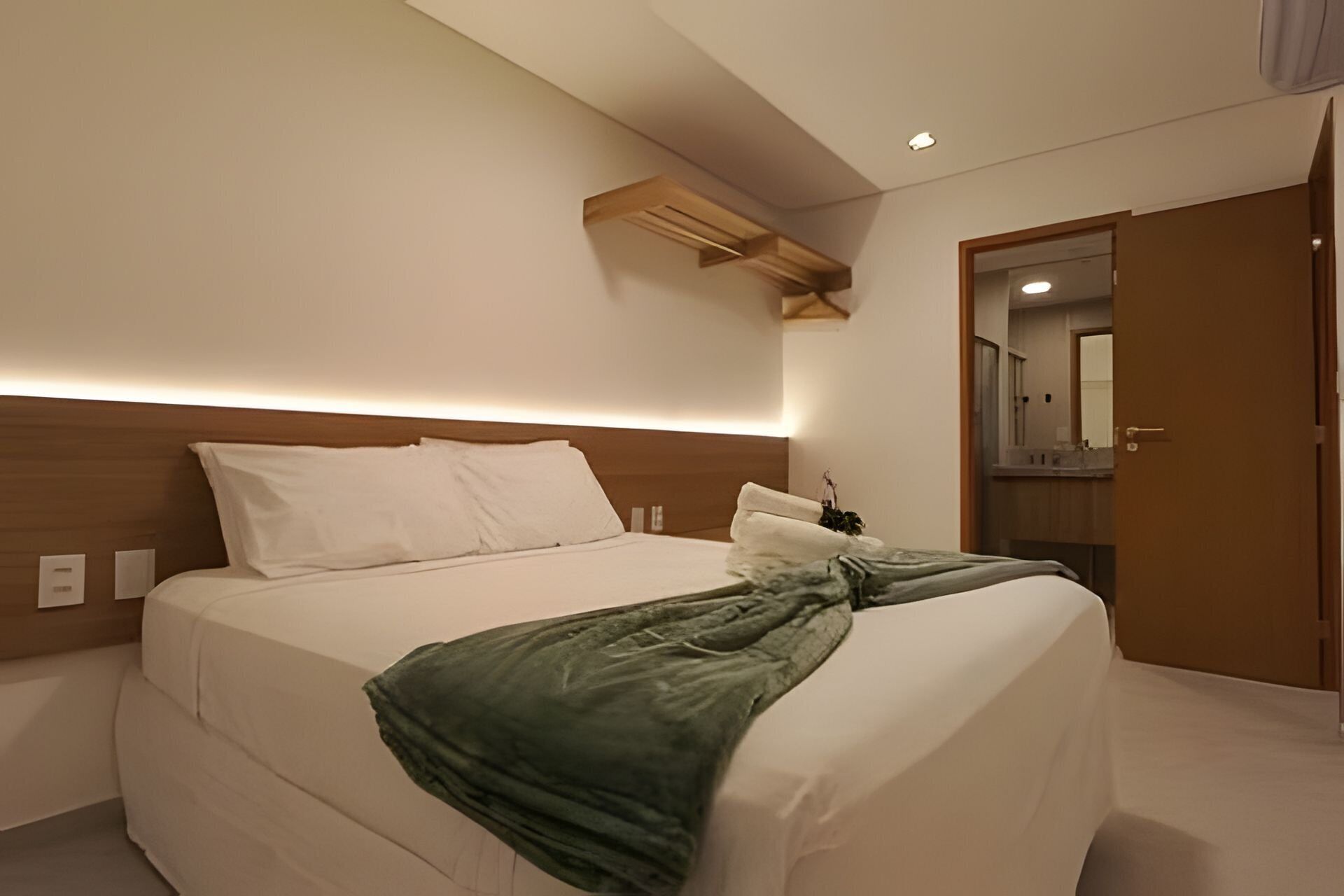 A hotel room with a bed, a wooden headboard, a nightstand, a mirror, and a door.