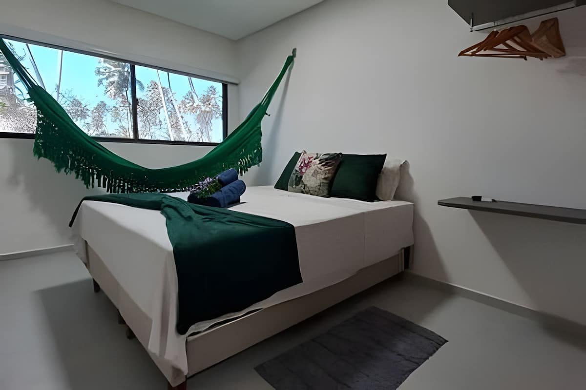 A bedroom with a bed, a hammock, a window, and a bedside table.