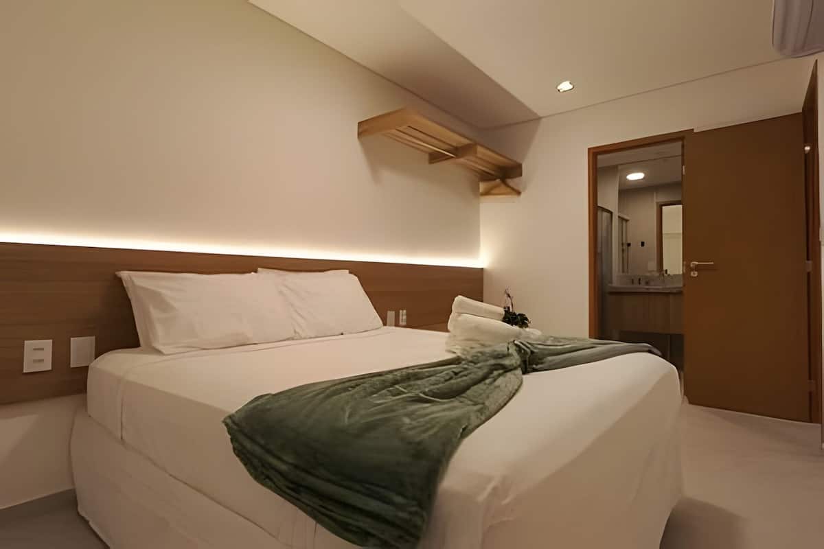 Habitación de hotel con cama, cabecera de madera, mesita de noche, espejo y puerta.