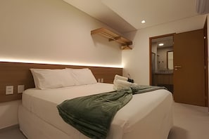 Habitación de hotel con cama, cabecera de madera, mesita de noche, espejo y puerta.