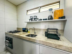A modern kitchen with a gas stove, double sink, and a countertop with a dish rack. - Cond em Resort Pe na Areia - By MME (Maceió)