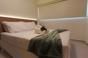 A neatly made bed with white linens, a green throw blanket, and a small potted plant.