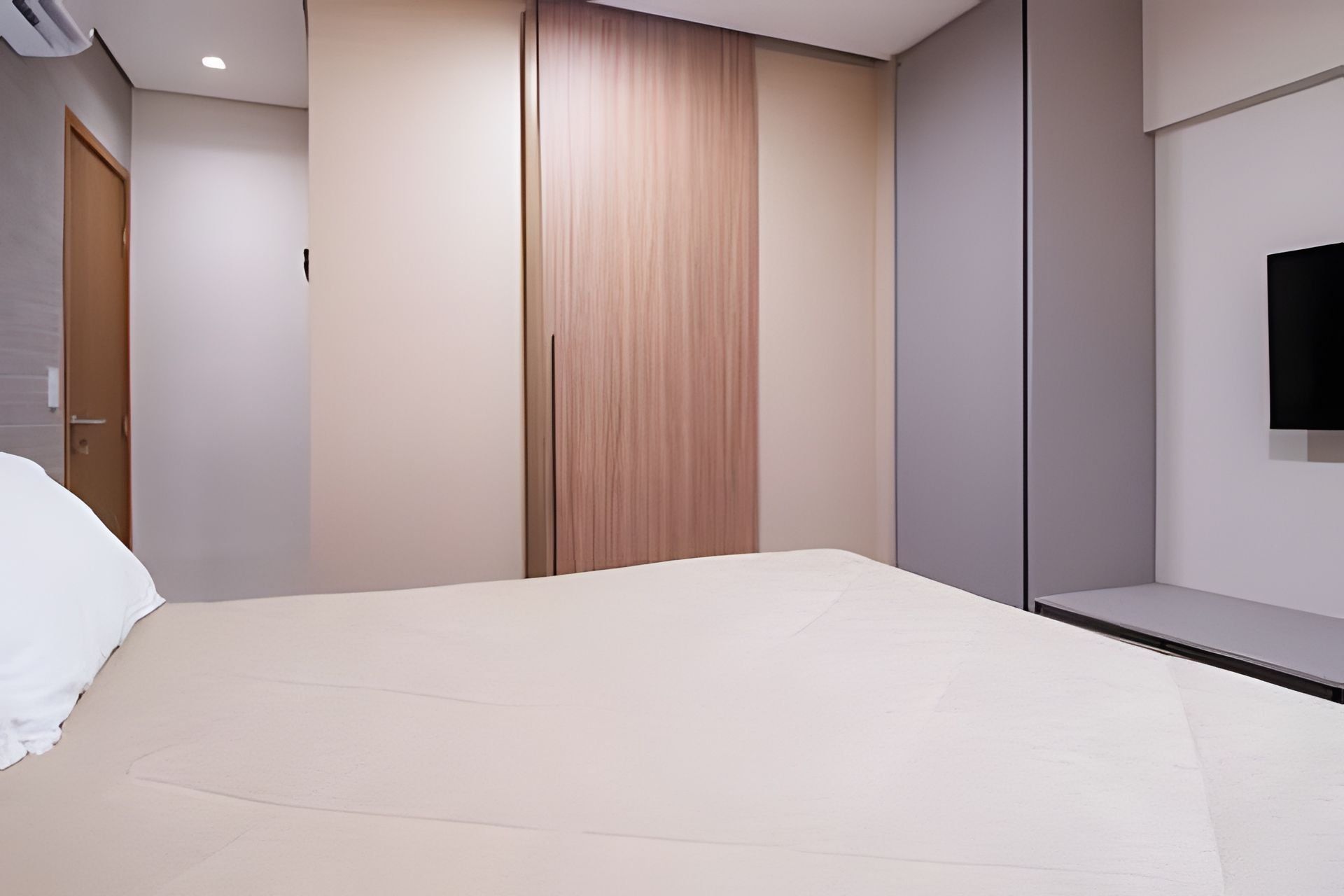 A modern bedroom with a bed, a wardrobe, and a television mounted on the wall.