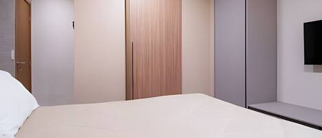 A modern bedroom with a bed, a wardrobe, and a television mounted on the wall.