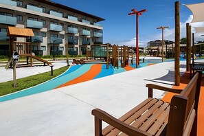 A modern outdoor area with a playground, benches, and a building with balconies.
