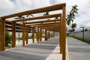 Een pad met houten balken erboven, palmbomen en een gebouw op de achtergrond.