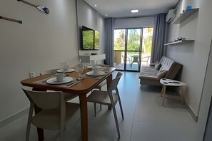 A modern dining area with a wooden table set for four, a sofa, and a TV mounted on the wall.