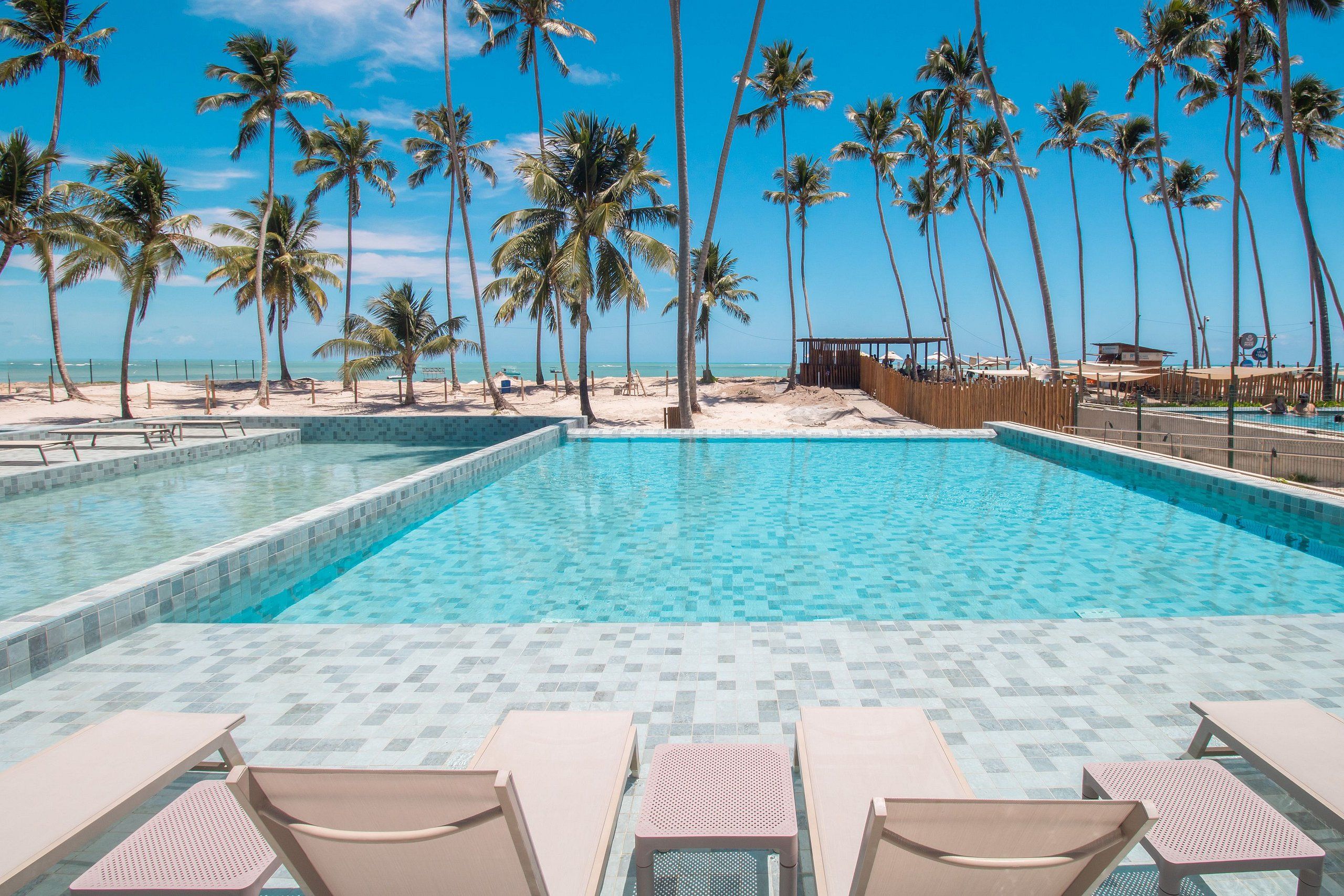 A pool with clear blue water, surrounded by lounge chairs and palm trees, with a view of the beach and ocean.