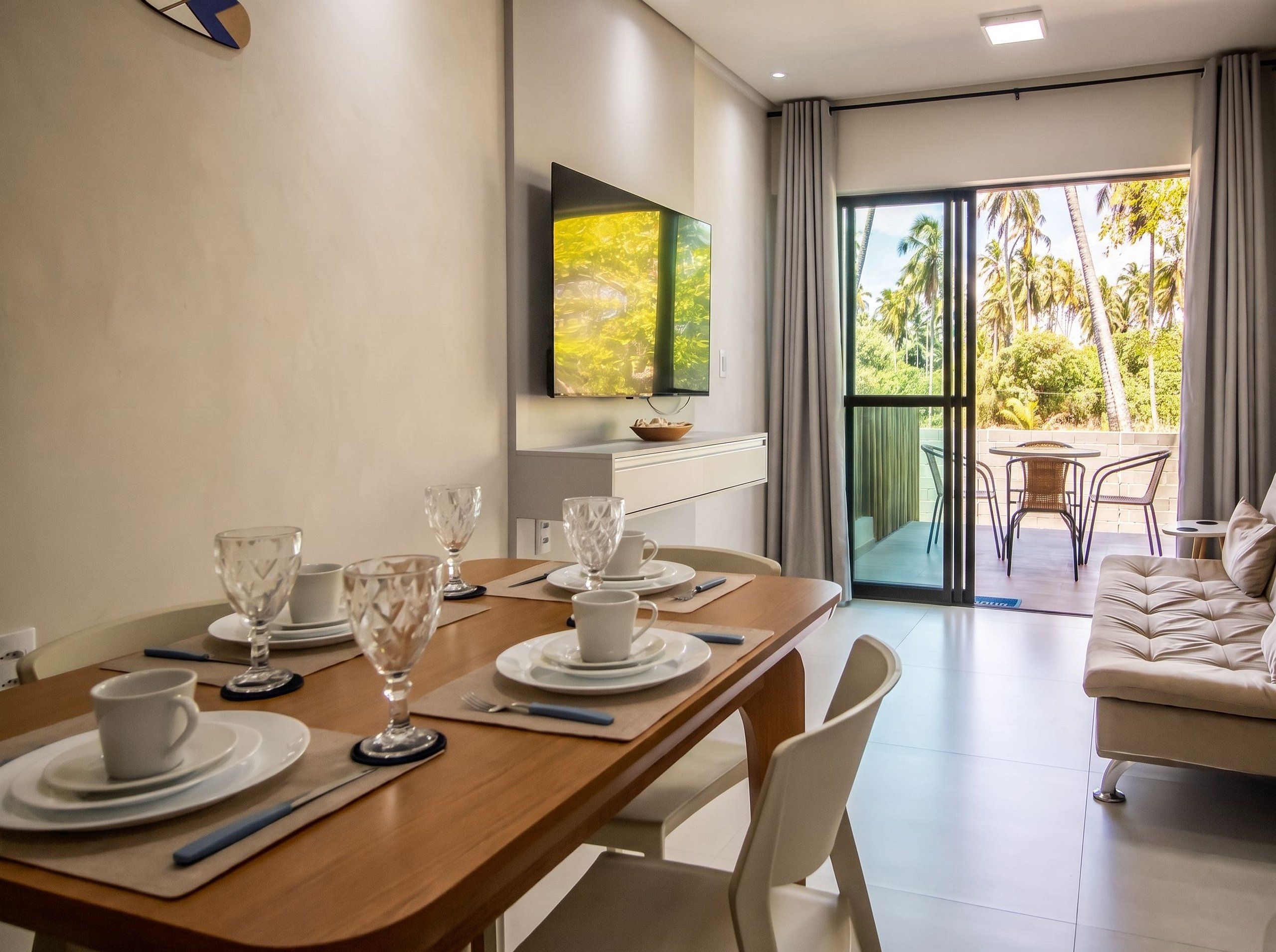 A dining area with a table set for four, a sofa, and a TV mounted on the wall.