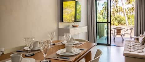 A dining area with a table set for four, a sofa, and a TV mounted on the wall.
