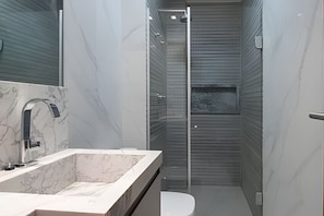Un baño moderno con lavamanos de mármol, cabina de ducha de vidrio y un inodoro.